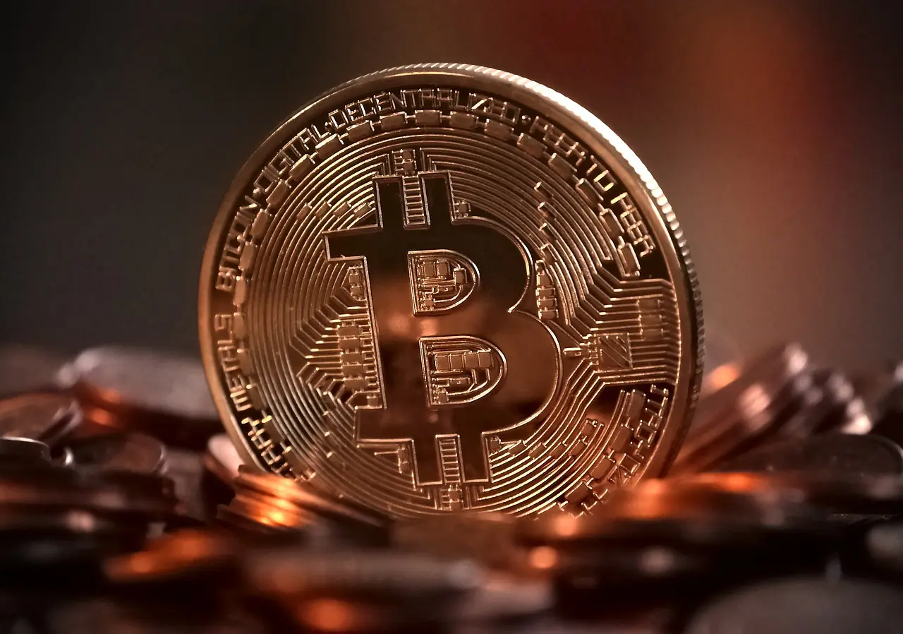 A close-up image of a prominent gold Bitcoin coin in sharp focus, with blurred cryptocurrency coins scattered in the background, all set against a warm, dark backdrop.