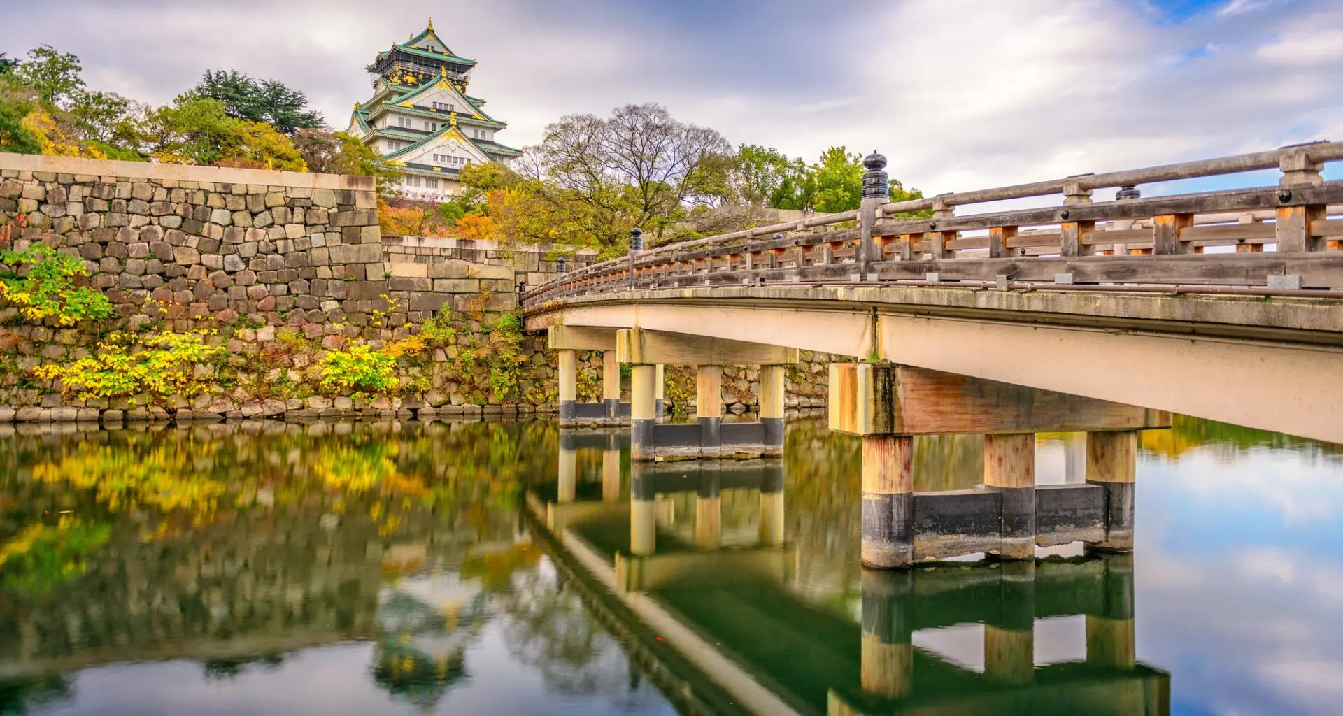 Osaka Castle reflected in the moat, with a traditional bridge in the foreground, during autumn in Osaka, Japan.