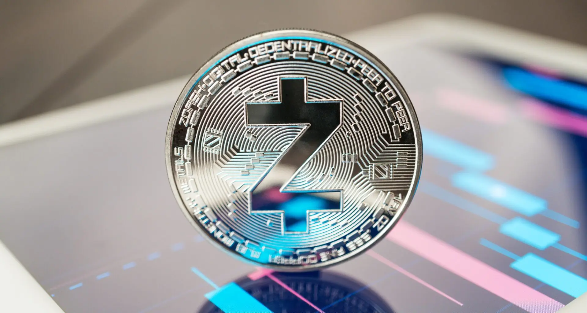 A silver-colored Zcash cryptocurrency coin, placed on a reflective surface with colorful digital patterns in the background.