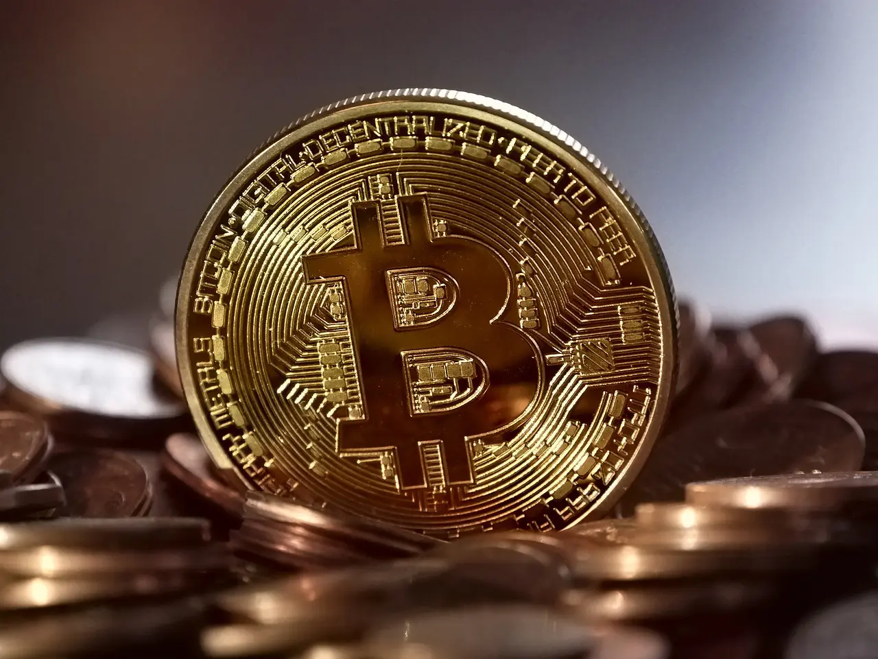 A gold Bitcoin token stands prominently in the foreground among various other coins.
