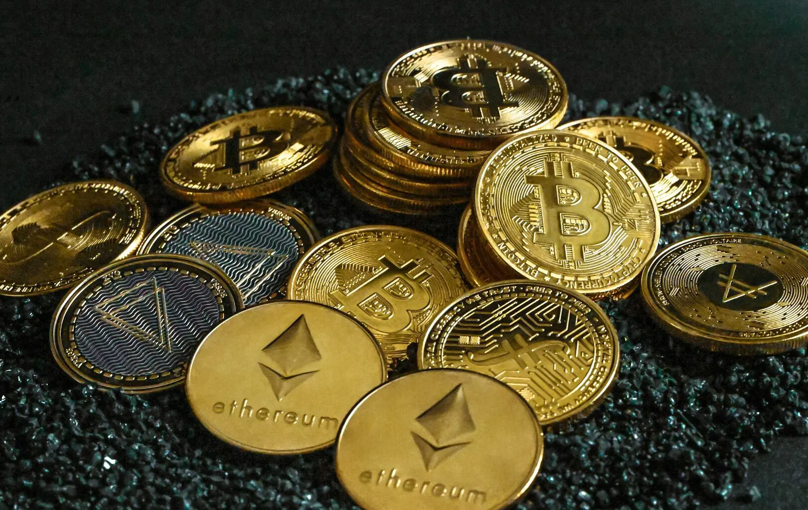 A pile of various cryptocurrency tokens, including gold and silver-colored coins.