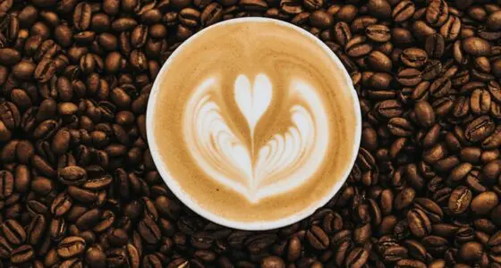 A cup of coffee with latte art in the shape of a heart sits on a bed of coffee beans.