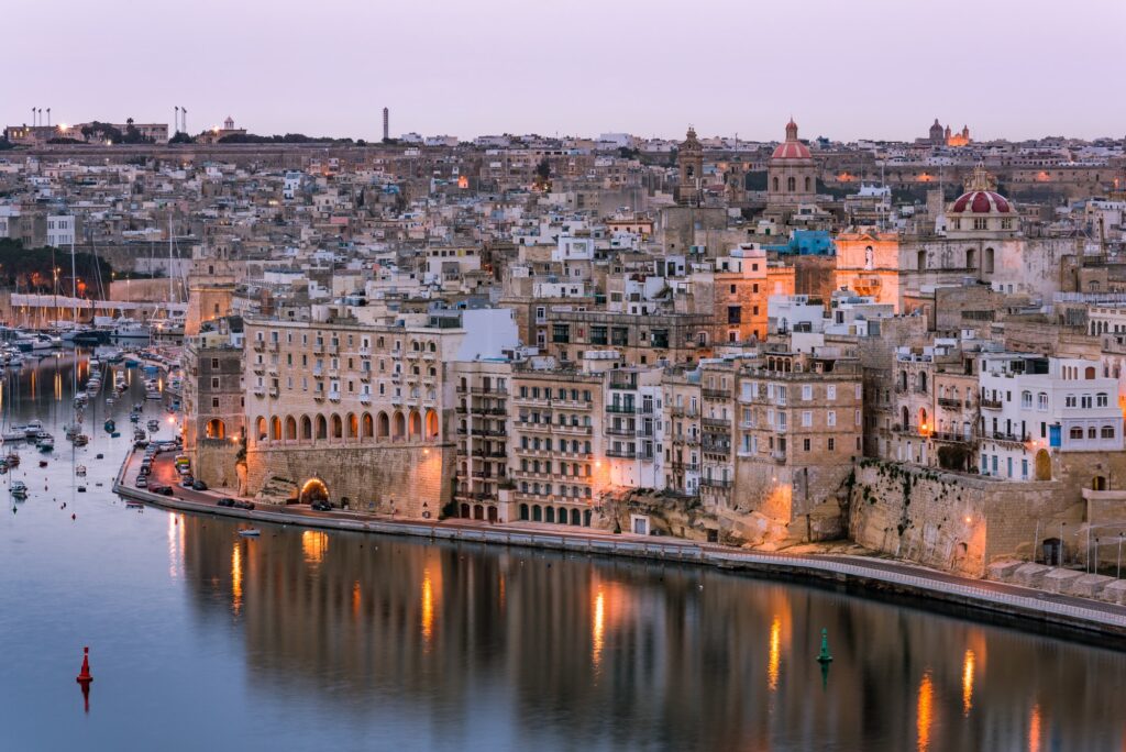 Twilight over Senglea and the Grand Harbor in Malta, with the city's historic buildings reflecting in the calm water.