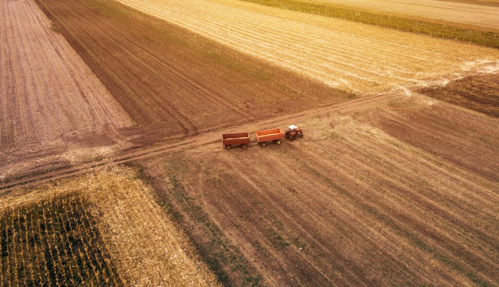 Aerial view of a tractor with two trailers on an agricultural field with distinct plowing patterns.