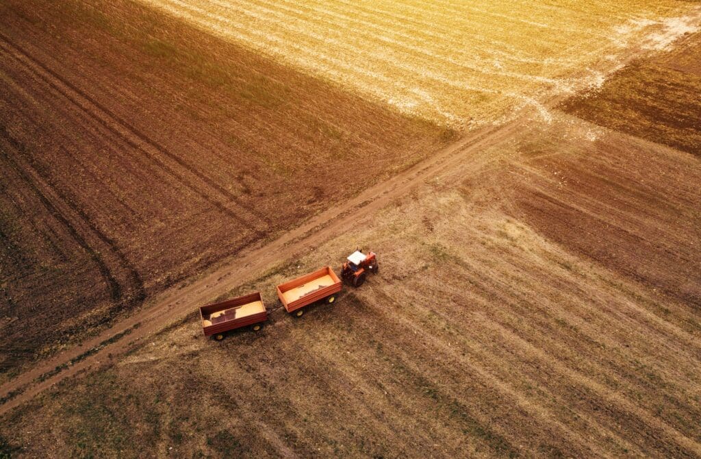 Aerial view of a tractor pulling two trailers in a harvested field.