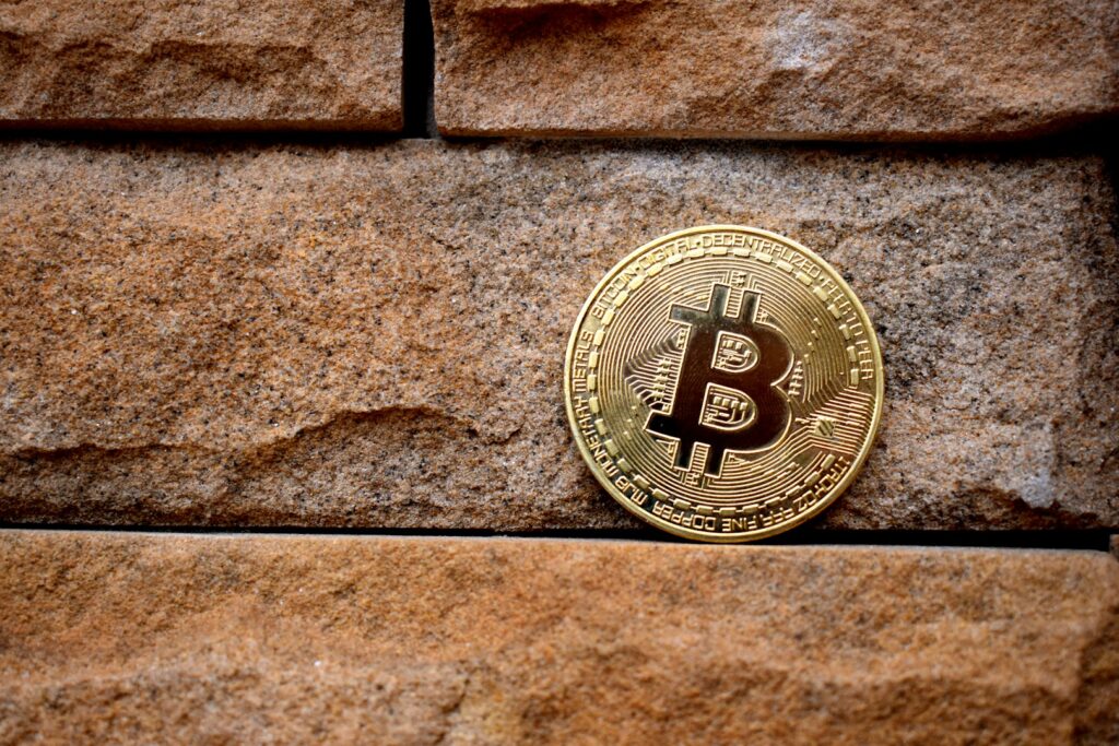 A gold Bitcoin sits on top of a red brick wall.
